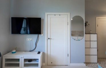 Contemporary interior of luxury apartment in grey tones. White door. TVand mirror on wall. White stand.