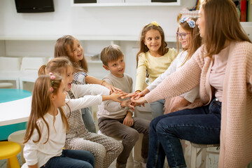Cute preschool kids put hands together with their nursery teacher
