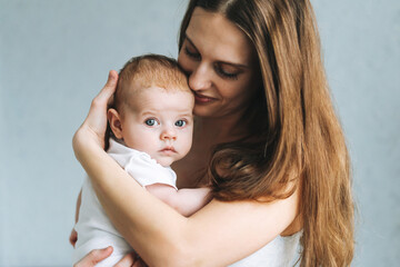 Portrait of young woman mom with long hair holding baby girl on hands at the home