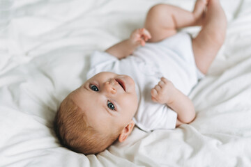 Cute baby girl 2-4 month on bed with white linen, natural tones, selective focus