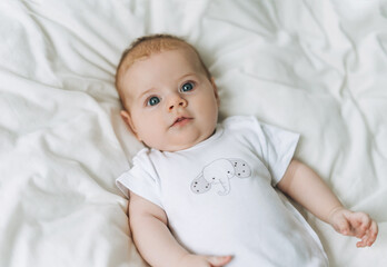 Cute baby girl 2-4 month on bed with white linen, natural tones, selective focus