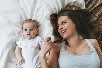 Young mother having fun with cute baby girl on the bed, natural tones, love emotion