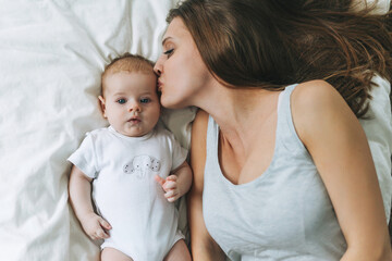 Young mother having fun with cute baby girl on the bed, natural tones, love emotion