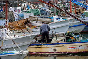 Fototapeta na wymiar 小さな漁港に停泊する漁船に乗り組み、漁の準備をする男性の後ろ姿