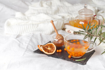 Autumn hot tea with ginger, lemon, honey and sea buckthorn on the bed