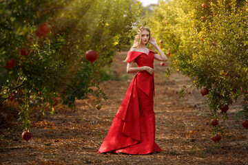 Beautiful young girl in long red dress in a pomegranate garden. Jewish New Year. Rosh Hashana concept
