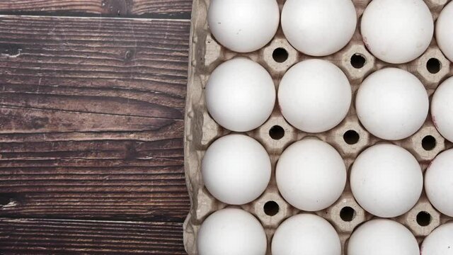 Rotating White Chicken Eggs In A Cardboard Box. Fresh Raw Eggs In A Paper Egg Container For Store And Shop. Egg Tray With Eggs On Wooden Table On Right Side. Top View.
