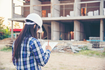 Woman construction engineer writing note wear plaid shirt safety white hard hat at construction...