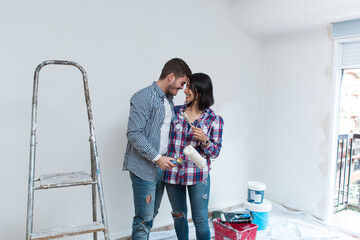 Loving couple smiling and working together on the remodeling of their home. Young couple embracing...