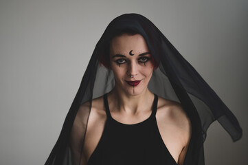 Redhead woman with a black veil on her head in a dark studio. A girl with an earring in her nose smiles slyly. Witch Makeup. Halloween costume.