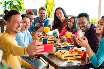 Friends group drinking cappuccino at coffee bar restaurant - People smiling and toasting juice while taking a selfie - Friendship concept with happy men and women at breakfast room.
