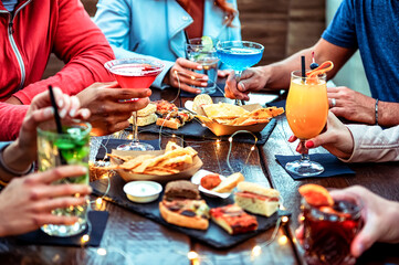 Group of friends enjoying appetizer drinking and eating in a bar - Close-up of hands of young...