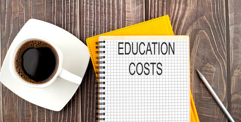 EDUCATION COSTS text on the notebook with coffee on wooden background