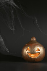Carved smiling pumpkin in gold color on a black background with cobwebs. The concept of Halloween decorations.