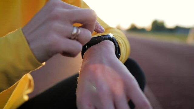 Fit woman use smart watch at sunset. Runner checking pulse on smartwatch on running workout. Modern technology and a healthy lifestyle. Athlete run woman check pulse on fitness bracelet.