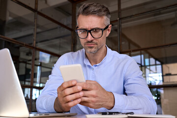 Mature business man entrepreneur holding smartphone using mobile apps looking at cell phone...