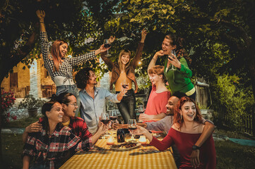 Multiracial friends enjoying dinner and drinking red wine in the garden - People having fun after...
