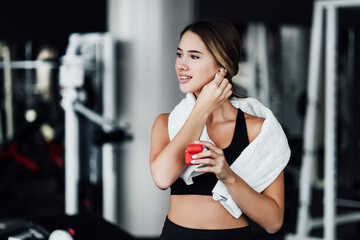 Attractive smiling girl enjoys her wireless headphones, she is in the gym during a workout, modern technology