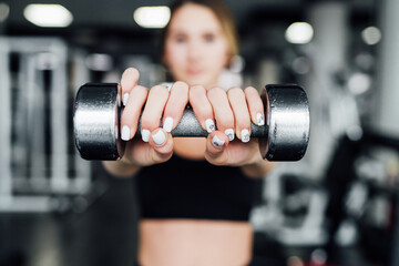 The focus is on the hand of a girl holding a dumbbell and pushing it into the camera