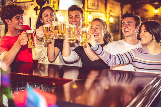 Group of happy people drinking and toasting beer at at the bar counter - Handsome teenager friends smiling while clink mugs of draft beer - Friendship and youth concept