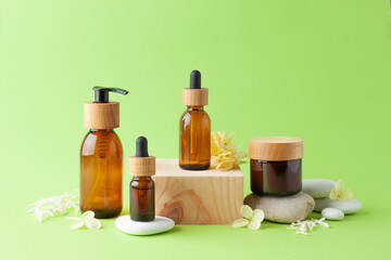 Cosmetic skin care products with wood podium and flowers, stone on green background. Close up, copy space