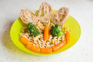 Funny meal idea. Vegetables with  rotini pasta and bread. Fusilli pasta on plate, broccoli and carrot. Funny food faces idea. 