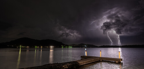 Wooden dock on the sea under a dark cloudy sky during the lightning at night