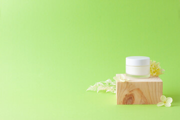 Jar of cosmetic cream with wood podium and flowers on green background. Close up, copy space