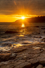 Obraz premium Acadia National Park, ME - USA - Oct. 13, 2021: Sunset vertical view of Ship Harbor at Acadia National Park in the Fall. Sunburst reflecting warm orange and yellow reflections on the surf.