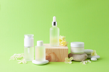 Obraz na płótnie Canvas Cosmetic skin care products with wood podium and flowers, stone on green background. Close up, copy space
