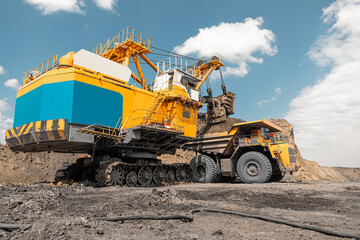 Large quarry dump truck. Big yellow mining truck at work site. Loading coal into body truck. Production useful minerals. Mining truck mining machinery to transport coal from open-pit production