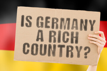 The question " Is Germany a rich country? " on a banner in men's hand. Money. Finance. Currency. Rate. Economy. Wealth. Salary. GDP. Million. Inequality. Economic. Income