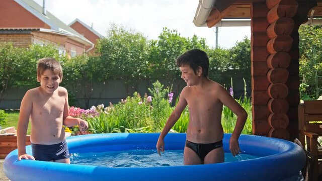 Two boys bathe and frolic in the pool in the summer, splashing water.
