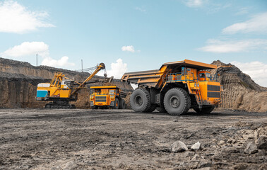 Large quarry dump truck. Big yellow mining truck at work site. Loading coal into body truck. Production useful minerals. Mining truck mining machinery to transport coal from open-pit production