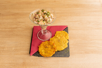 Fototapeta na wymiar Peruvian shrimp ceviche with purple onion and parsley on a glass glass accompanied by patacones for dipping