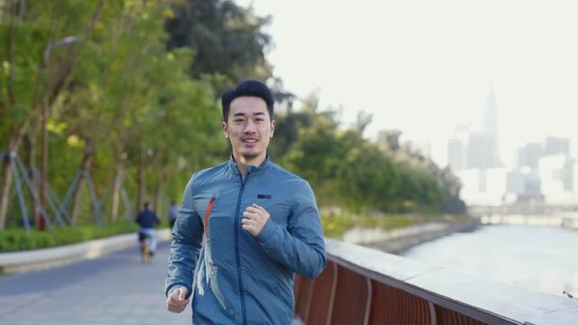young asian man running exercising outdoors in city park by a river
