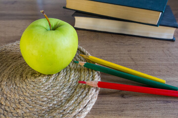 green apple on a wicker napkin against the background of books with colored pencils