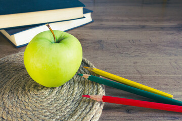 green apple on a wicker napkin against the background of books with colored pencils