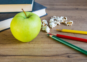 green apple on a wicker napkin against the background of books with colored pencils
