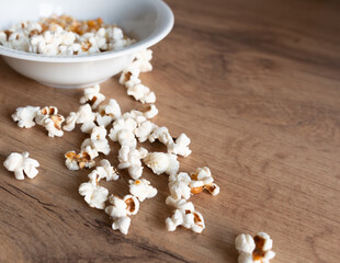 Fried popcorn and beans lies in a white plate and scattered a row on a wooden table