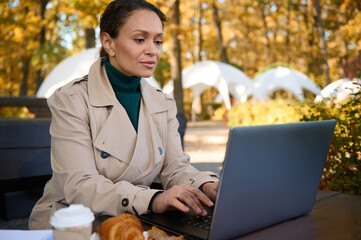 African American business woman typing on laptop in a forest cafe while enjoying remote work in the...