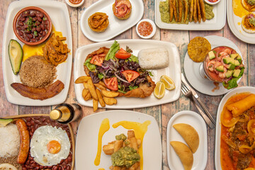 set of delicious Colombian food recipes on wooden table with paisa tray, patacones, chicharrones, fried yucca with guacamole, prawn cocktail and corn arepas