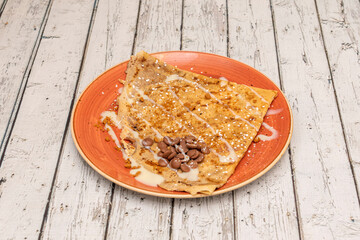 Sweet crepe with dark chocolate syrup and white chocolate, icing sugar on a red plate