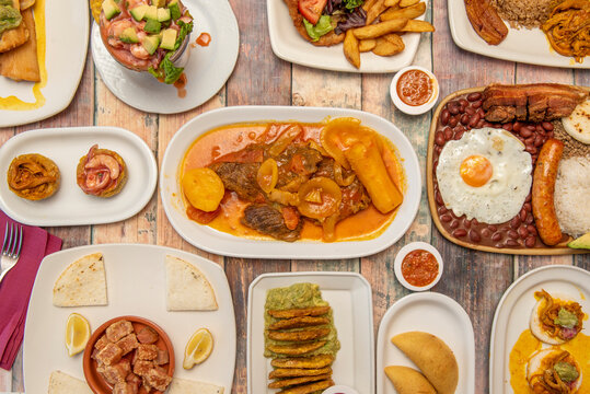 Top view image of a set of Colombian food dishes, with valluna cutlet, empanadas, paisa tray, prawn cocktail, fried patacones, shredded meat and guacamole