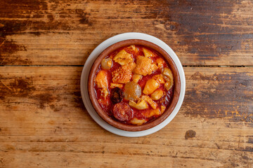 Spanish tapas of tripe a la madrileña with chorizo, bacon and blood sausage in a clay casserole on wooden table