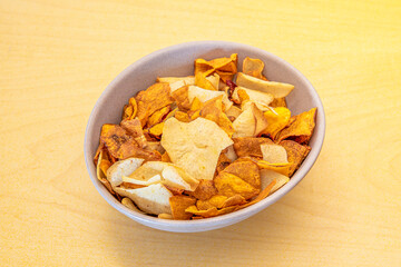 Appetizers bowl of potato chips, sweet potatoes, plantains and other vegetables on yellow table