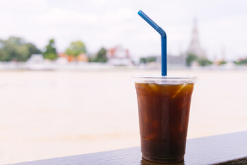 Iced Americano coffee on wooden table with Wat Arun temple in the background.