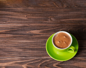 Green cup with coffee on a wooden background. Top view, place for text