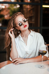 blonde girl with red lips in a white blouse in a snake skirt in sunglasses in a red beret with a glass of wine in a restaurant in a relaxing atmosphere