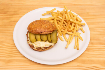 Pulled pork burger with lots of pickled gherkins and melted cheese with bread and sesame seeds and poppies garnished with French fries